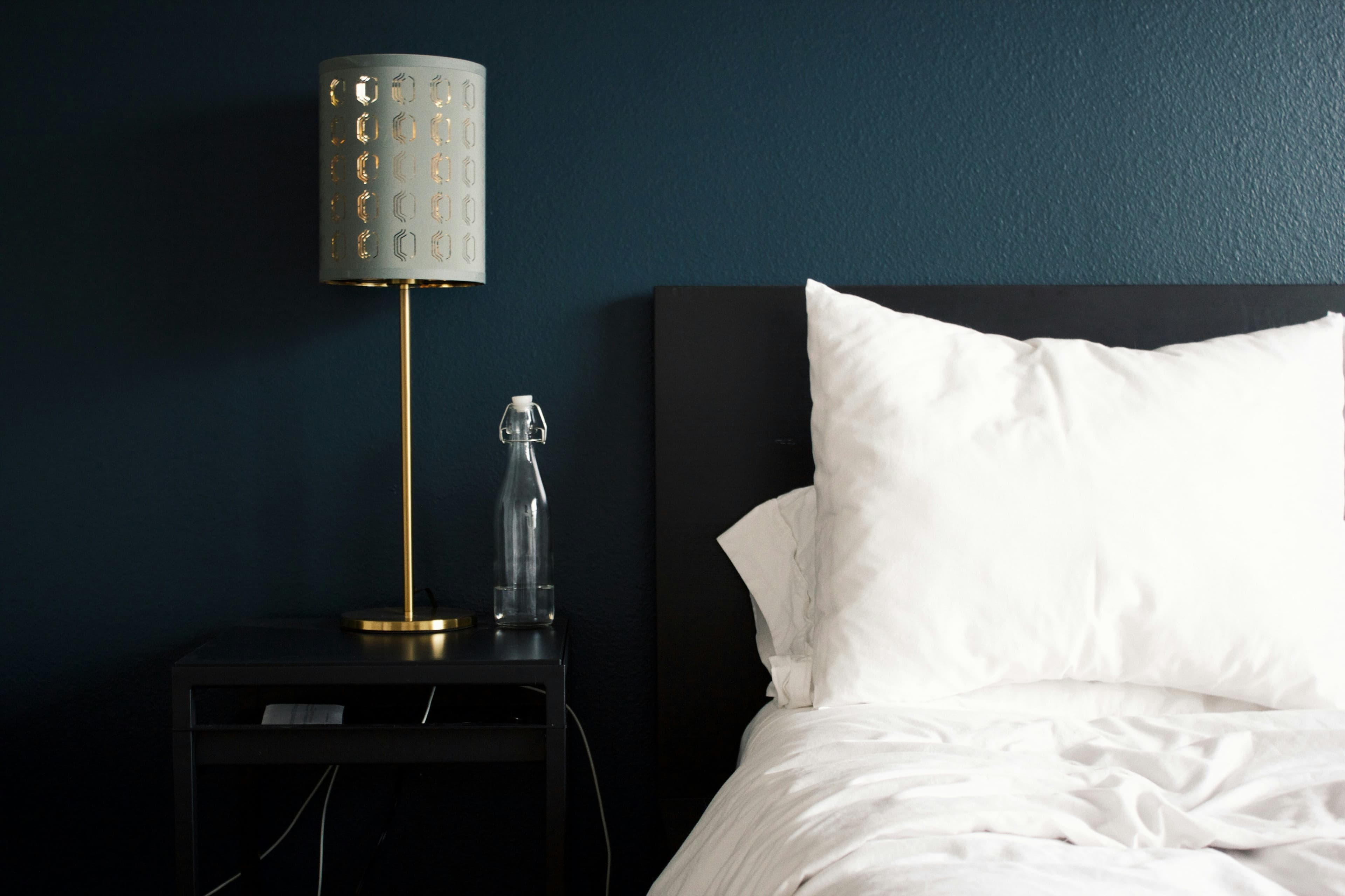 A made hotel bed beside a bedside lamp and a water bottle