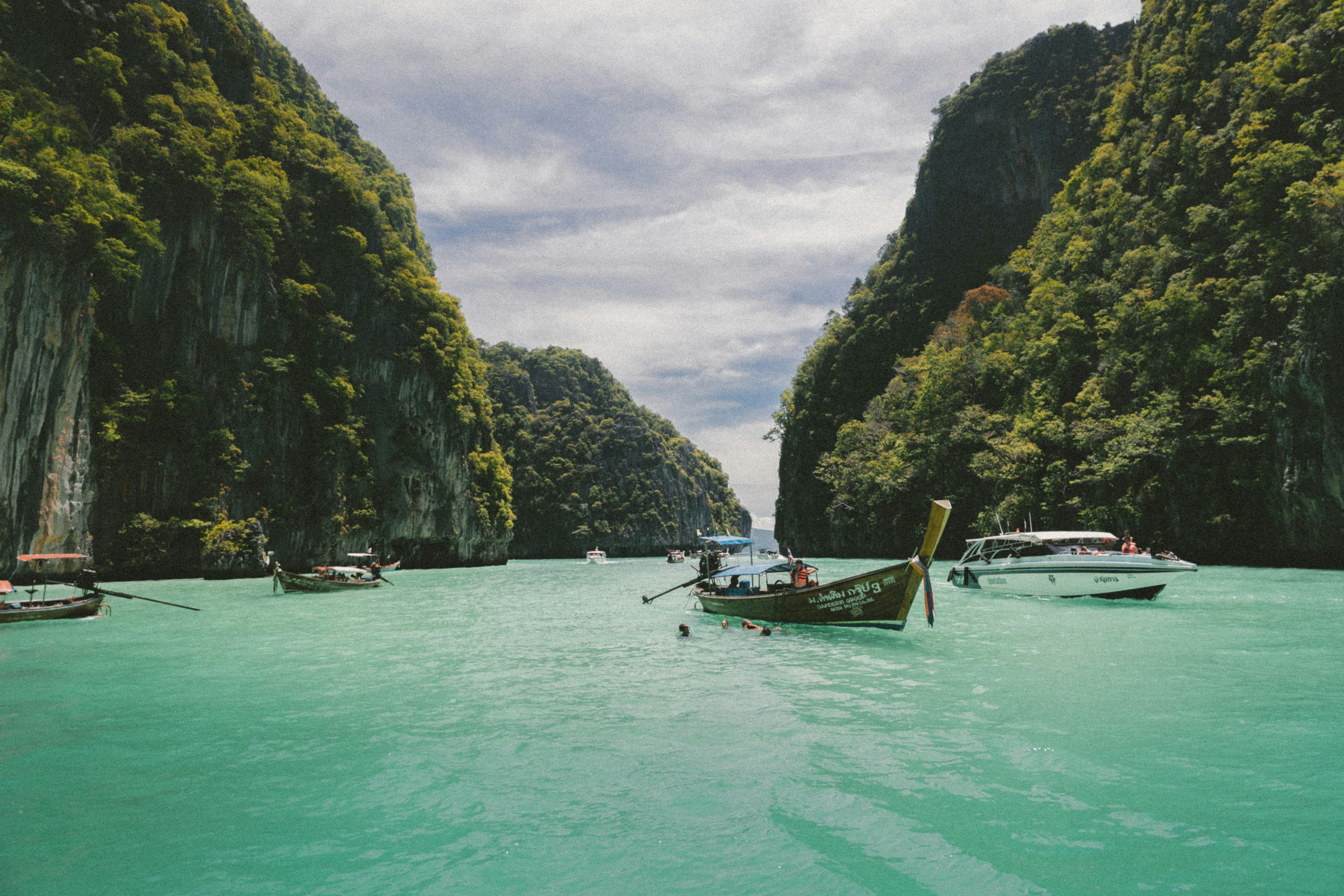 A longtail boat in a turquoise bay between cliffs