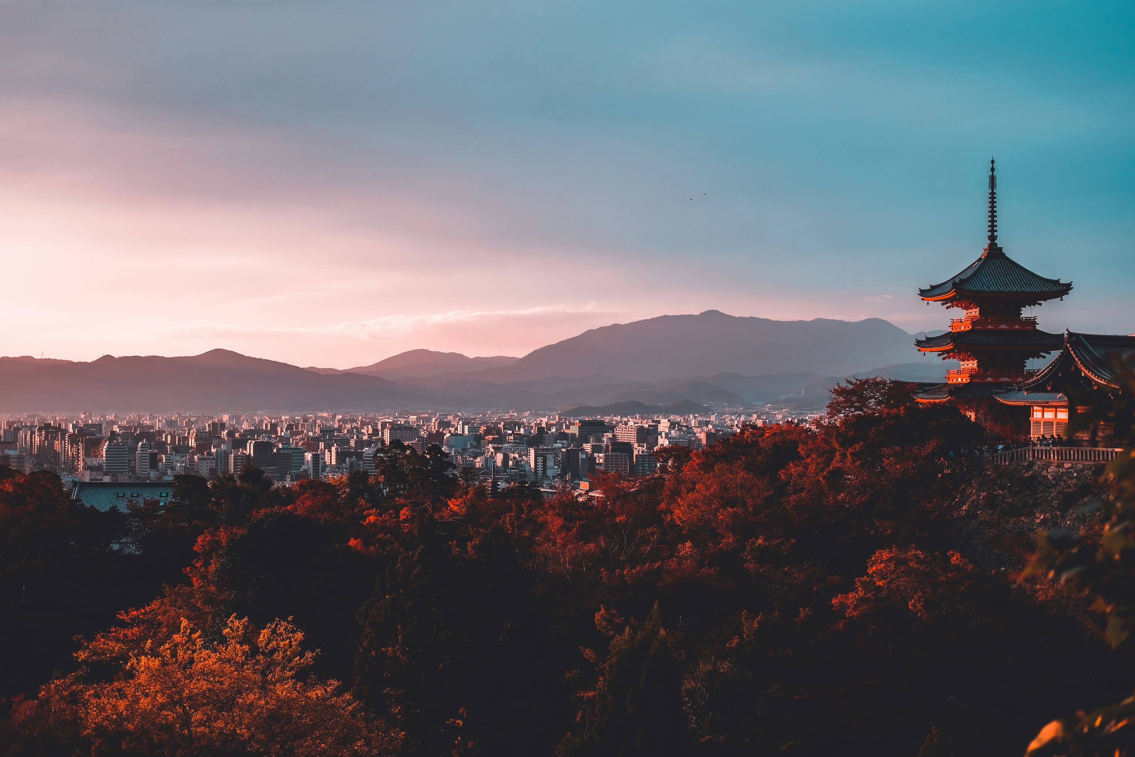 A pagoda rising above autumn trees in Kyoto with mountains beyond