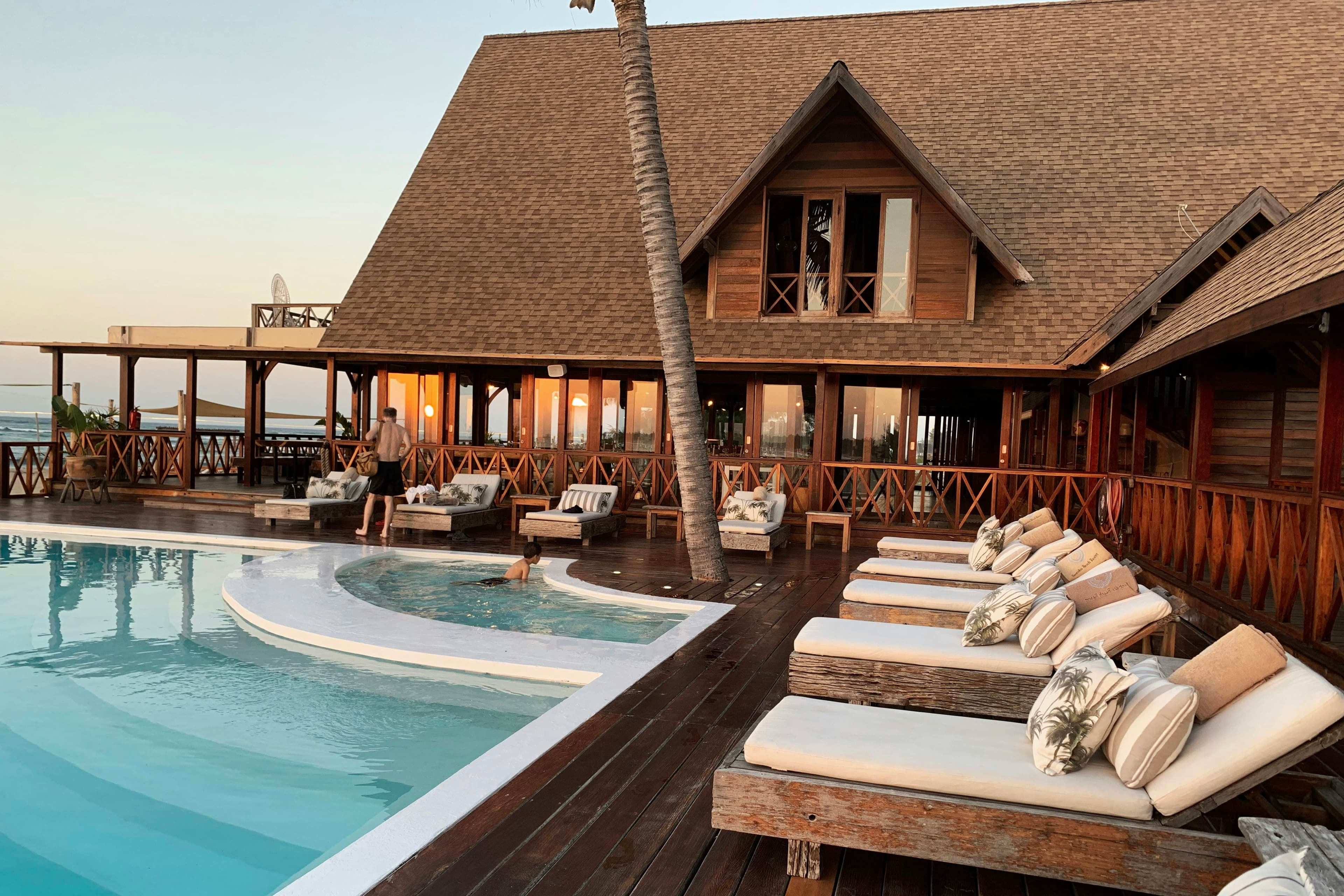 A timber lodge beside a pool with sun loungers