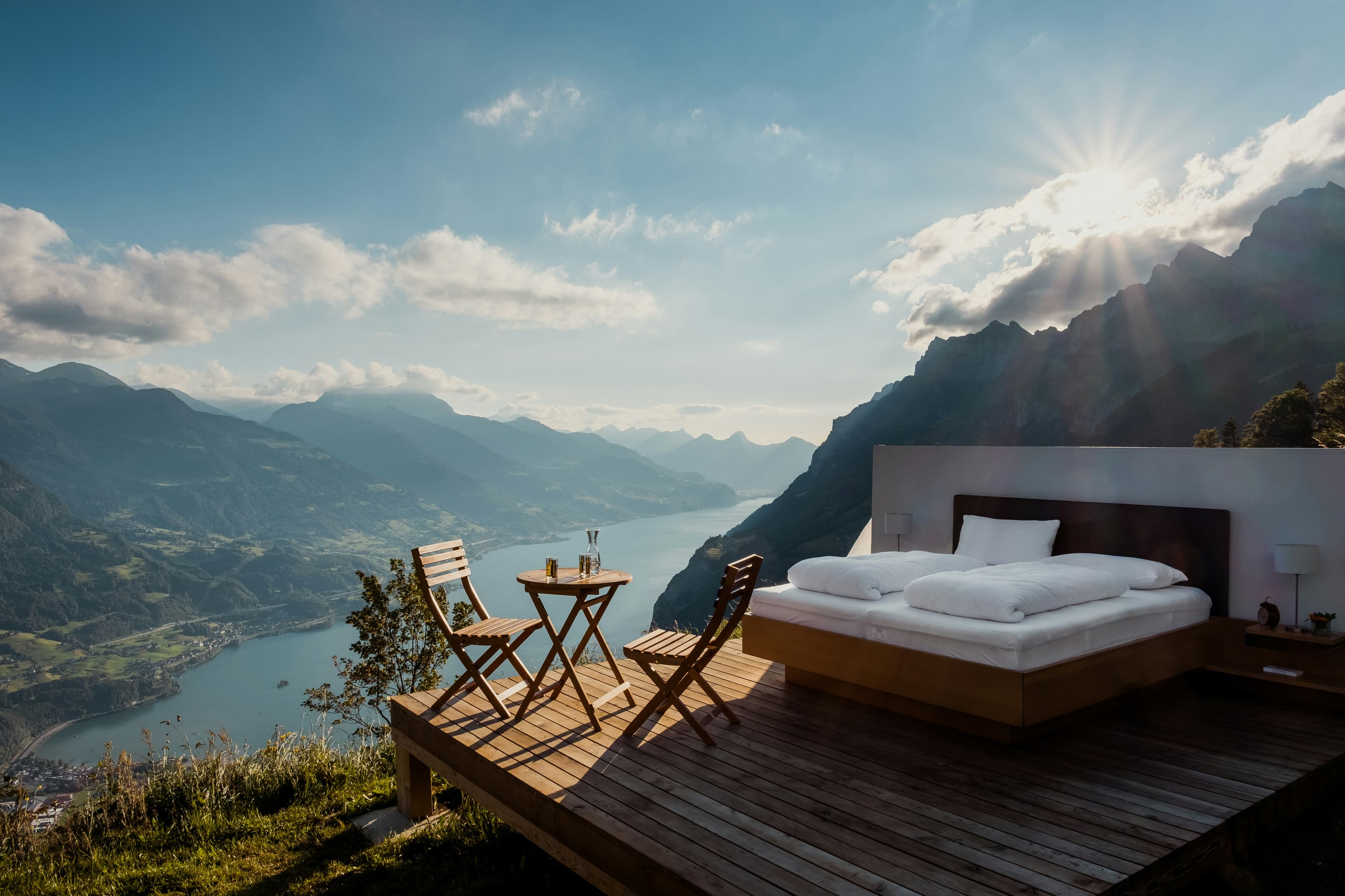 A bed on a terrace above a lake and mountains