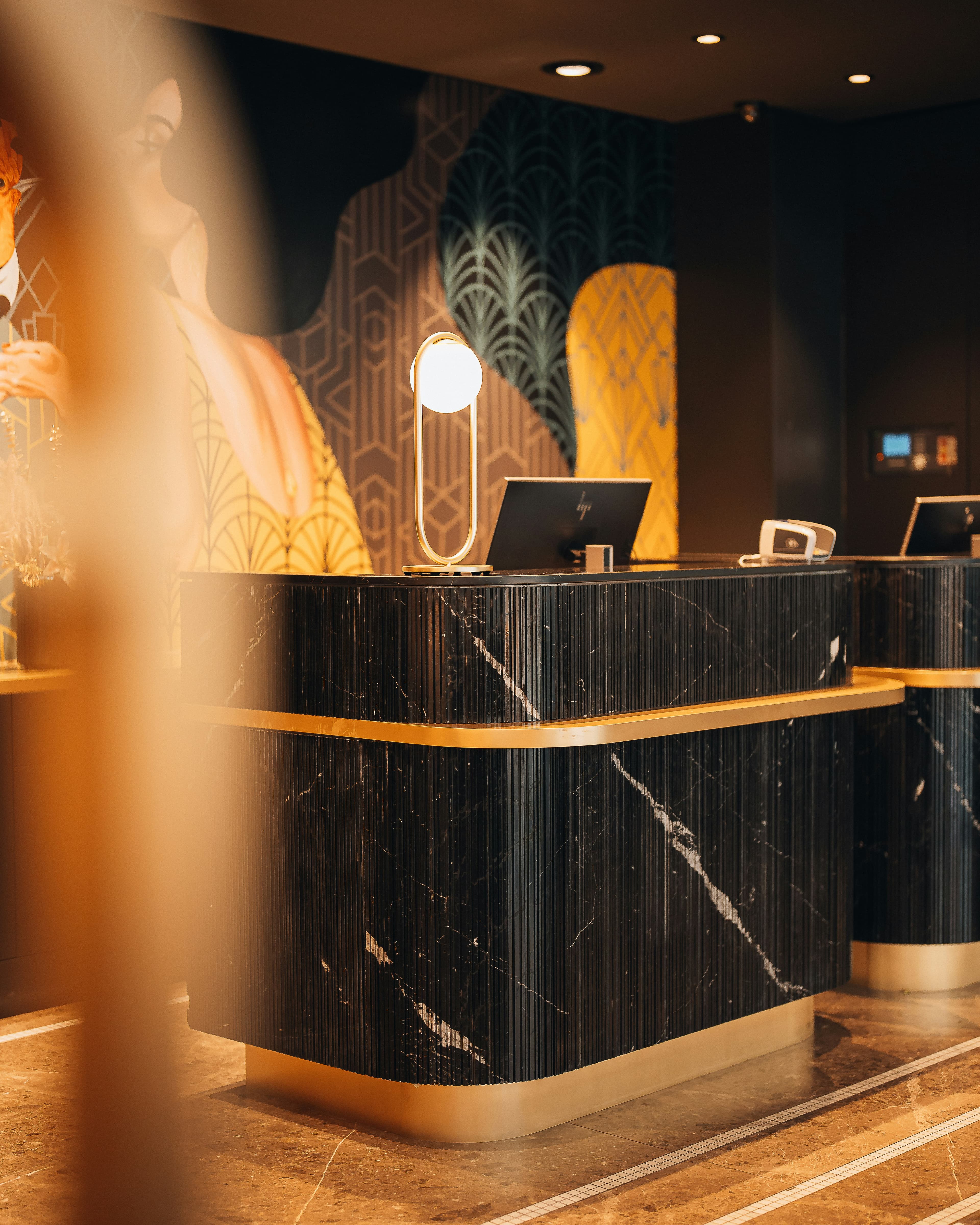 A black marble reception desk with gold trim in a softly lit hotel lobby