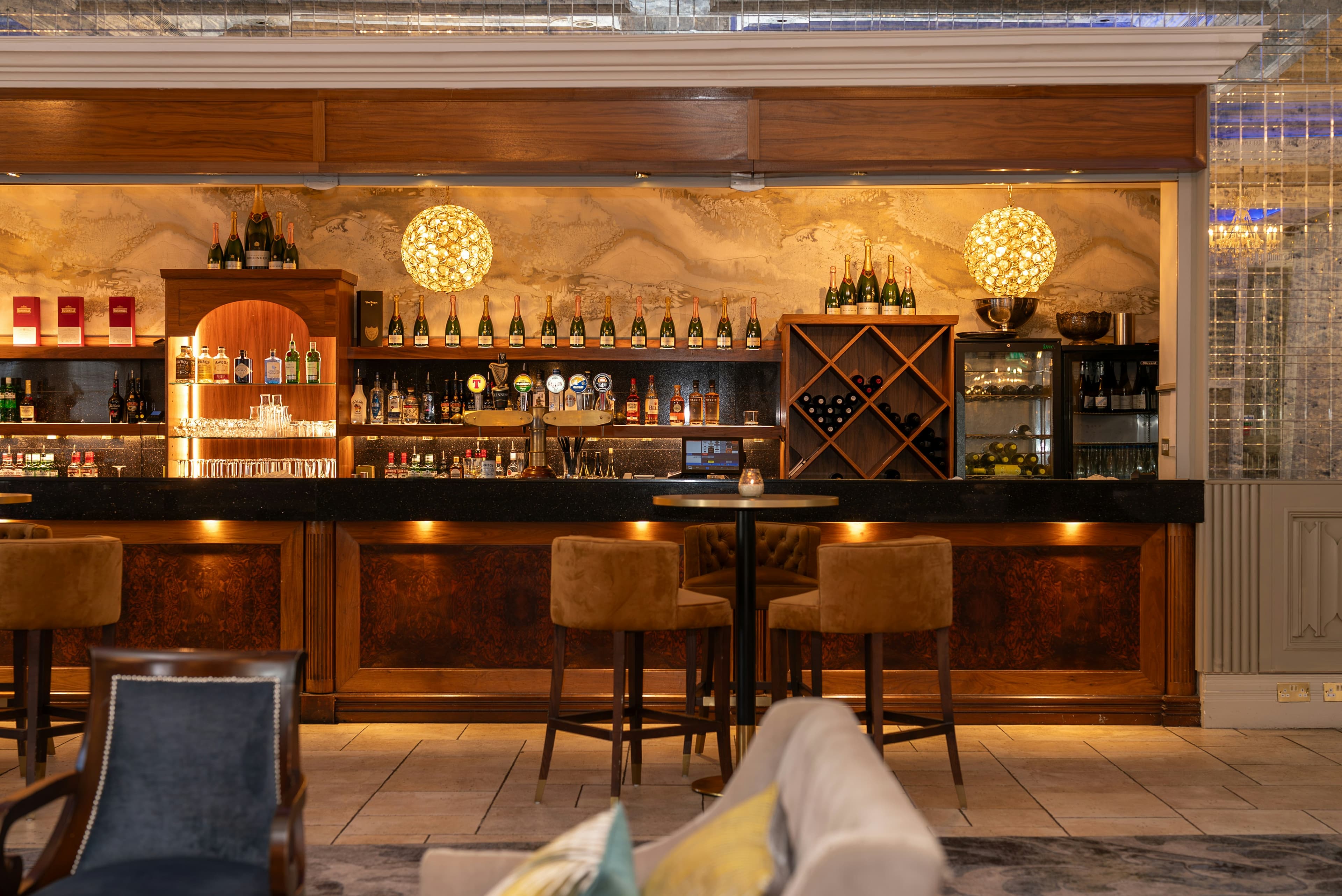 A hotel bar with stools, warm pendant lights and shelves of bottles